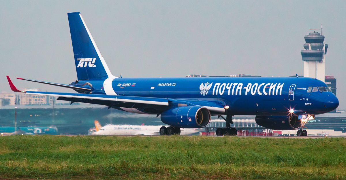 Blue Russian Postal Service plane on airport tarmac with control tower in the background.