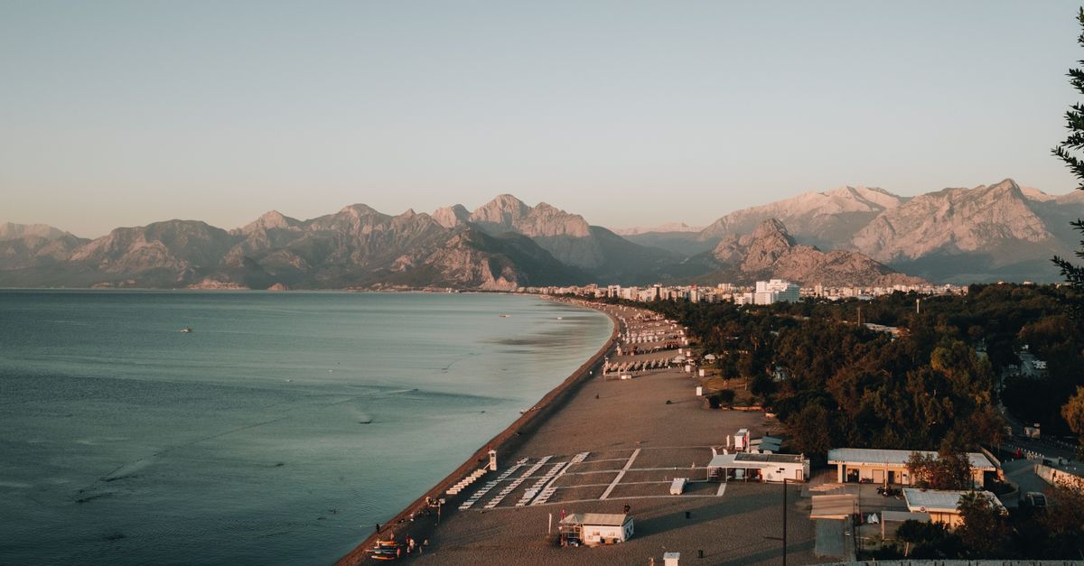 Explore Antalya's beautiful coastline with mountains, beach, and resort town at dawn.