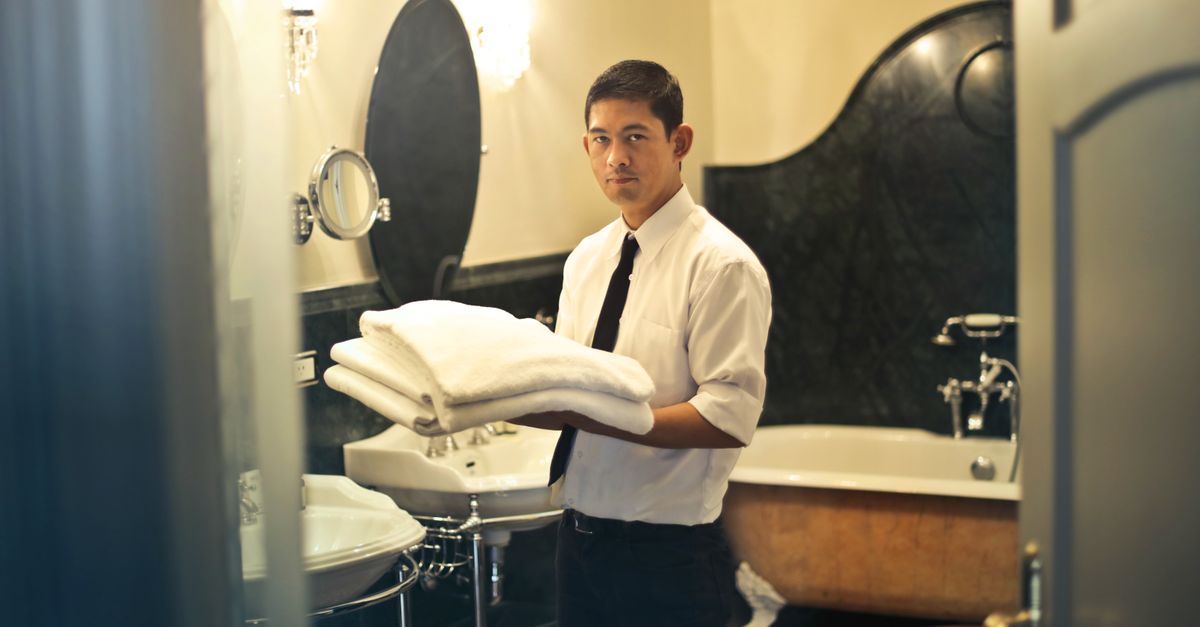 A hotel employee holding towels in a luxury bathroom with elegant decor.