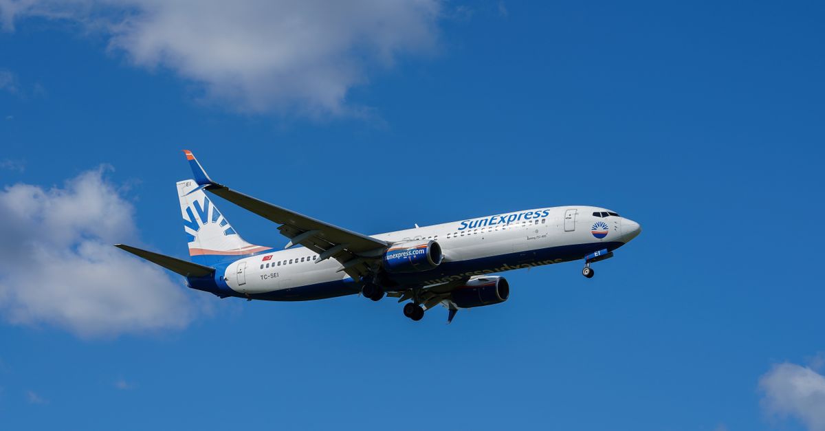 A SunExpress airplane in flight approaching Hamburg Airport under a clear blue sky.