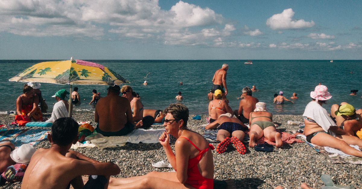 A vibrant scene of people relaxing and sunbathing on a pebbled beach in Sochi, Russia.