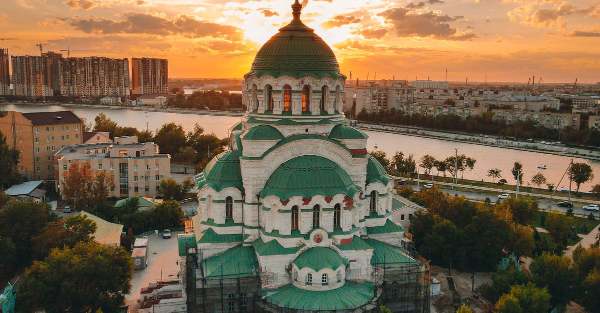 A stunning cathedral with green domes at sunset beside a river, showcasing architectural beauty.