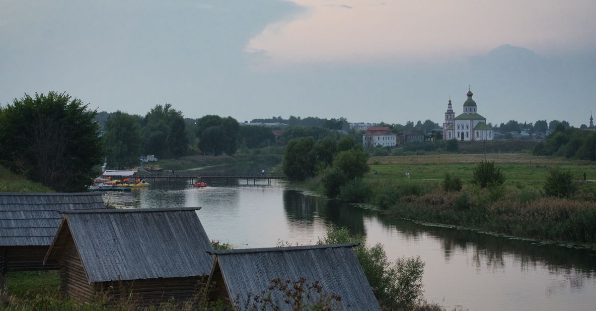 Scenic view of Suzdal's countryside with river and orthodox church at dusk.