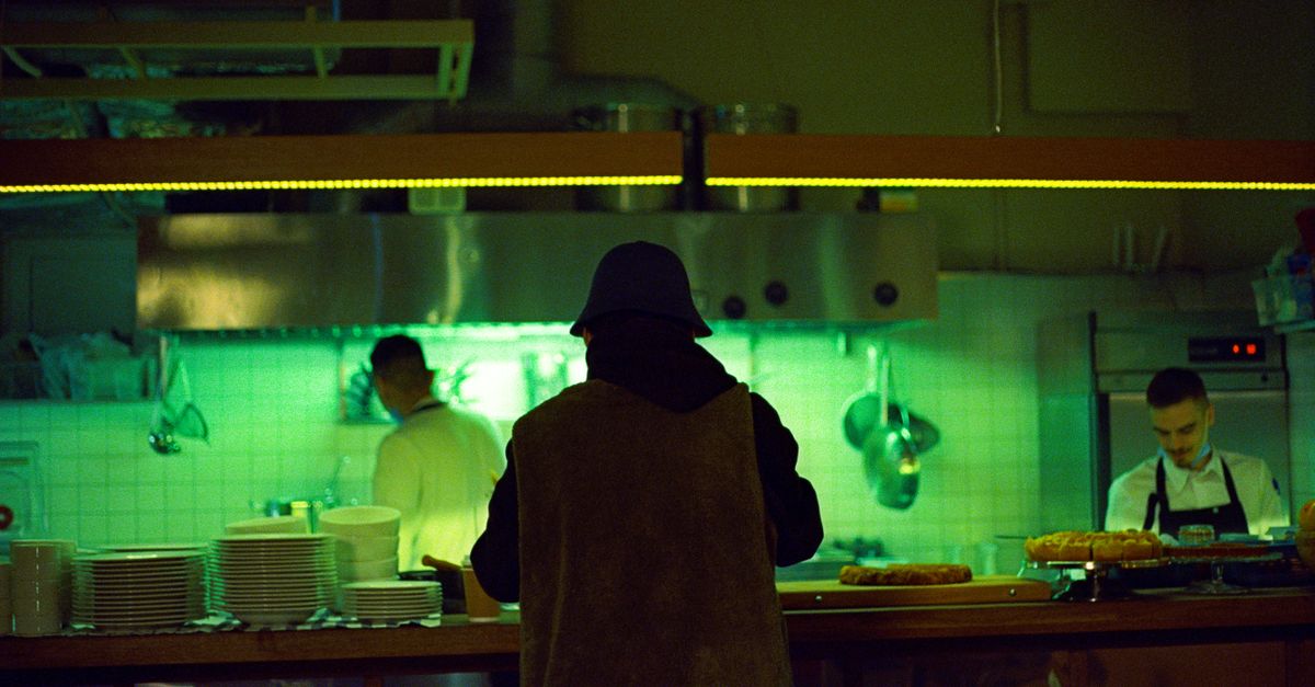 Chefs preparing dishes in a vibrant restaurant kitchen with a neon ambiance in Moscow.