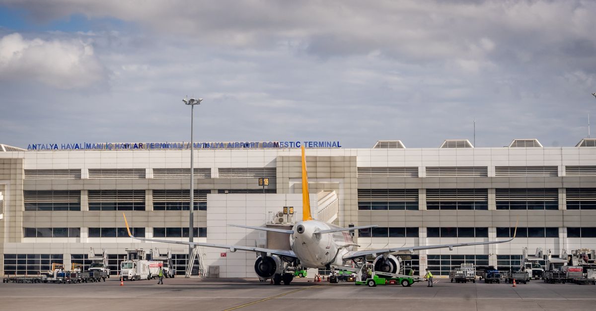 Airplane parked at Antalya Airport with terminal building in the backdrop under cloudy skies.