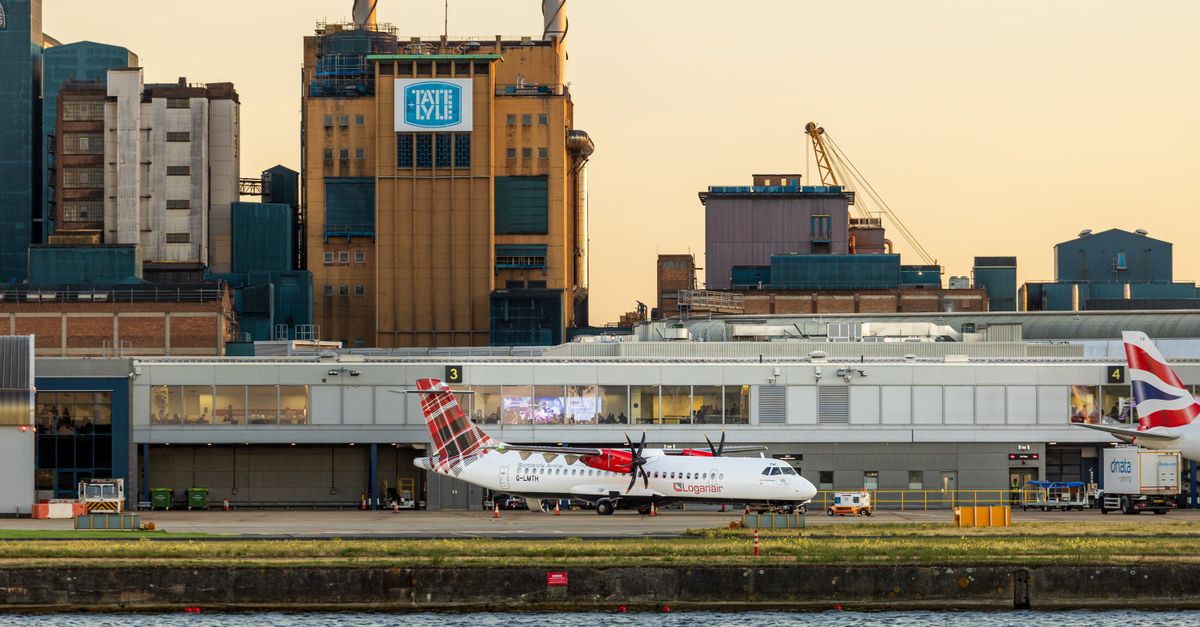 View of airplanes parked at London City Airport with industrial buildings in the background at sunset.