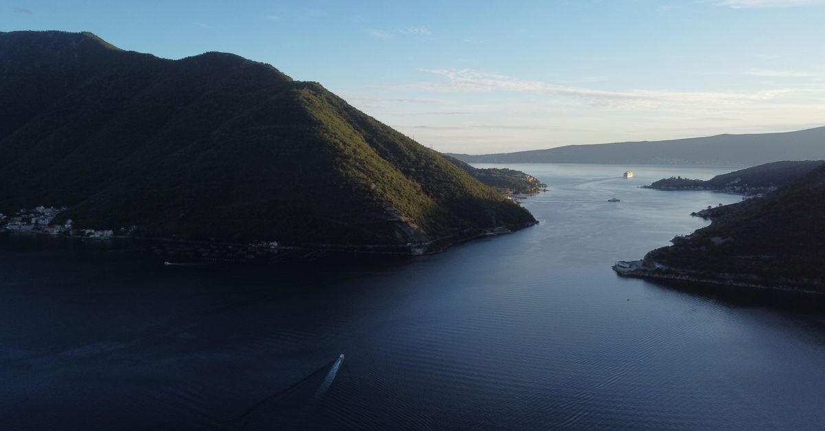 A breathtaking aerial view of Perast Bay, Montenegro with mountains, sea, and a cruise ship at sunset.