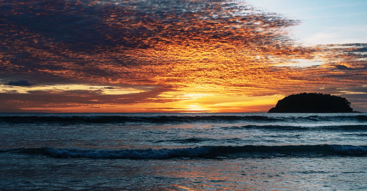 A breathtaking sunset over a Phuket beach with vivid colors and ocean waves, creating a serene and atmospheric scene.