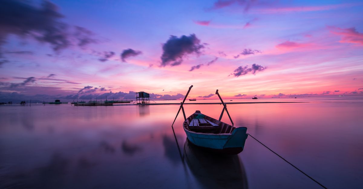 A tranquil tropical sunrise with a lone boat on calm waters.